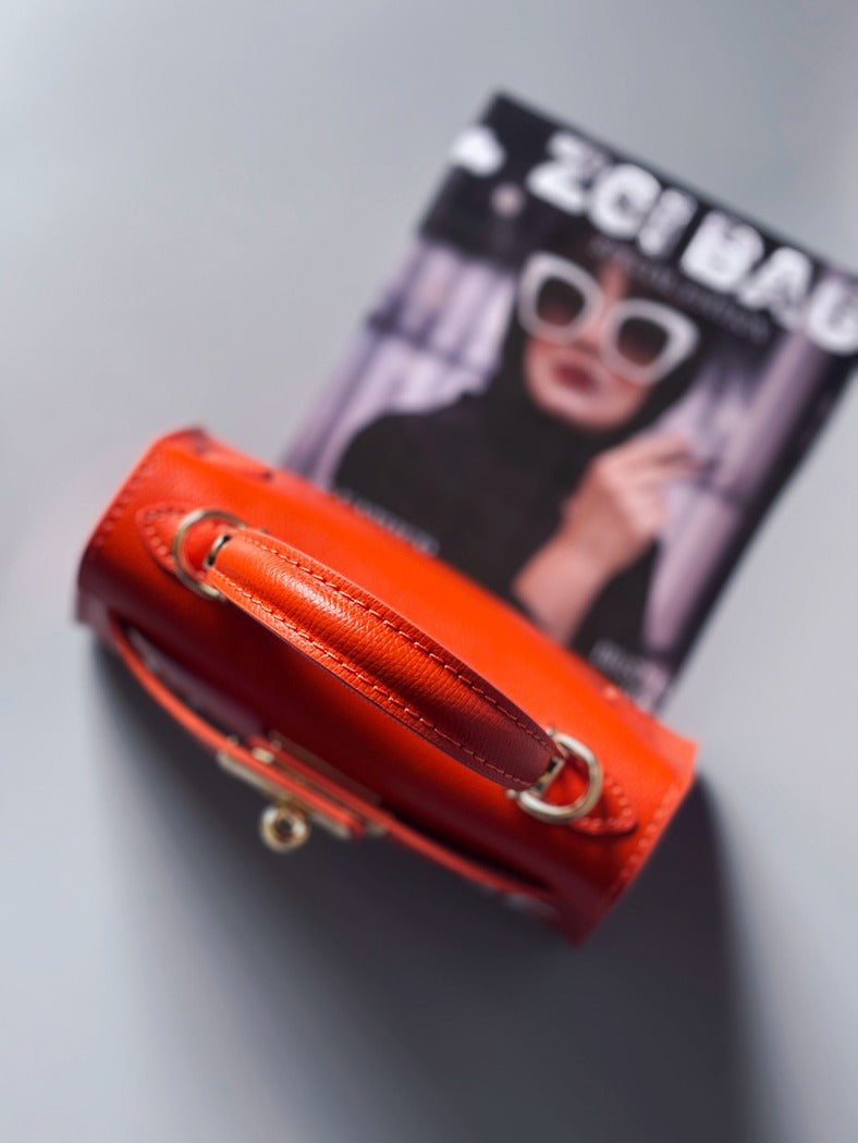Designová luxusní oranžová kabelka s ručně psaným nápisem, elegantním otočným zámkem a odnímatelným crossbody popruhem.