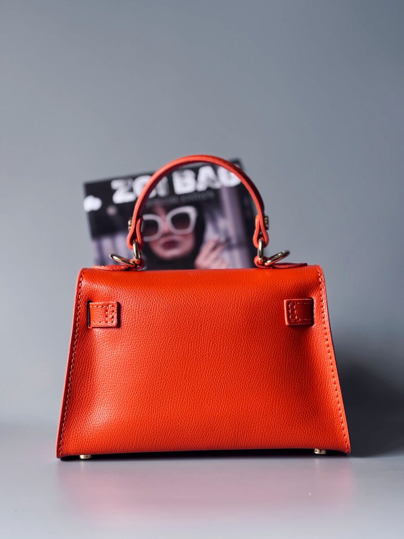 Designová luxusní oranžová kabelka s ručně psaným nápisem, elegantním otočným zámkem a odnímatelným crossbody popruhem. Zezadu.