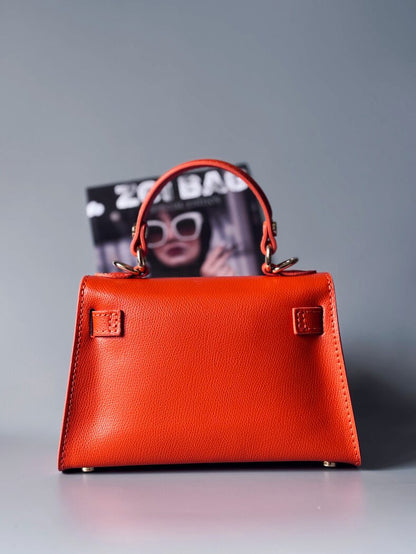 Designová luxusní oranžová kabelka s ručně psaným nápisem, elegantním otočným zámkem a odnímatelným crossbody popruhem. Zezadu.