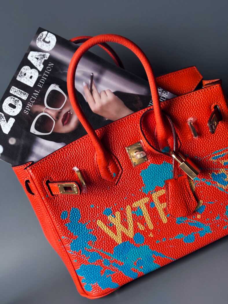 Oranžová kožená kabelka Zoi Bag s ručně psaným nápisem "WTF" a modrými cákanci barvou. Zapínání pomocí zlatého zámku s klíčkem.
