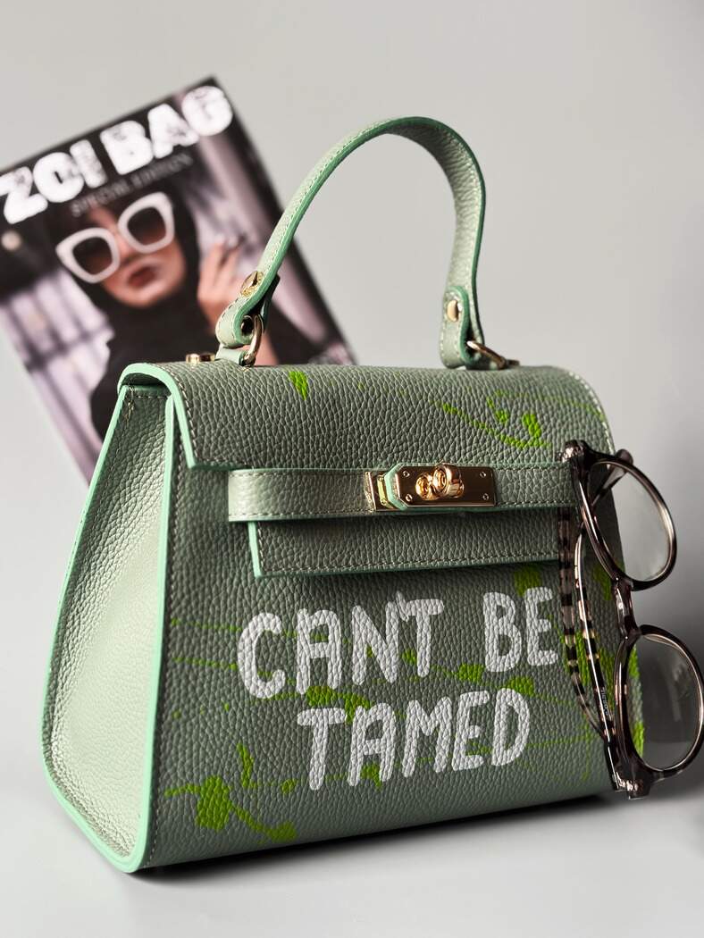 Designová pistáciová kožená kabelka Zoi Bag s ručně psaným nápisem a s cákanci barvou. Zapínání pomocí otočného zlatého zámku.