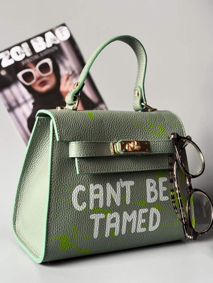 Designová pistáciová kožená kabelka Zoi Bag s ručně psaným nápisem a s cákanci barvou. Zapínání pomocí otočného zlatého zámku.