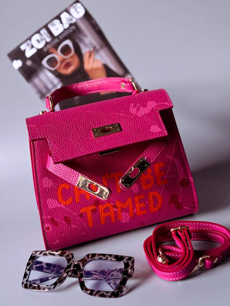Designová růžová kožená kabelka Zoi Bag s ručně psaným nápisem a s cákanci barvou. Zapínání pomocí otočného zlatého zámku.