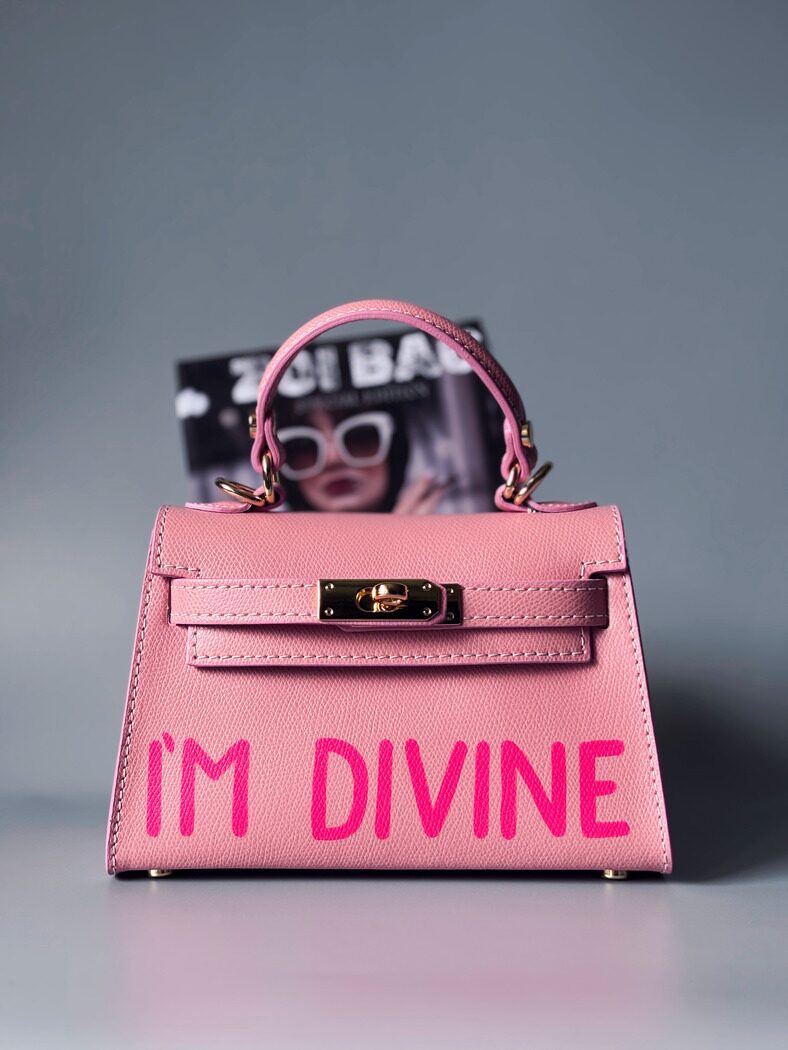 Designová luxusní růžová kabelka s ručně psaným nápisem, elegantním otočným zámkem a odnímatelným crossbody popruhem.