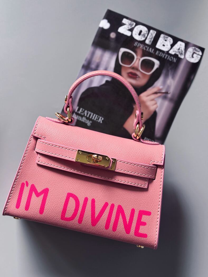 Designová luxusní růžová kabelka s ručně psaným nápisem, elegantním otočným zámkem a odnímatelným crossbody popruhem.