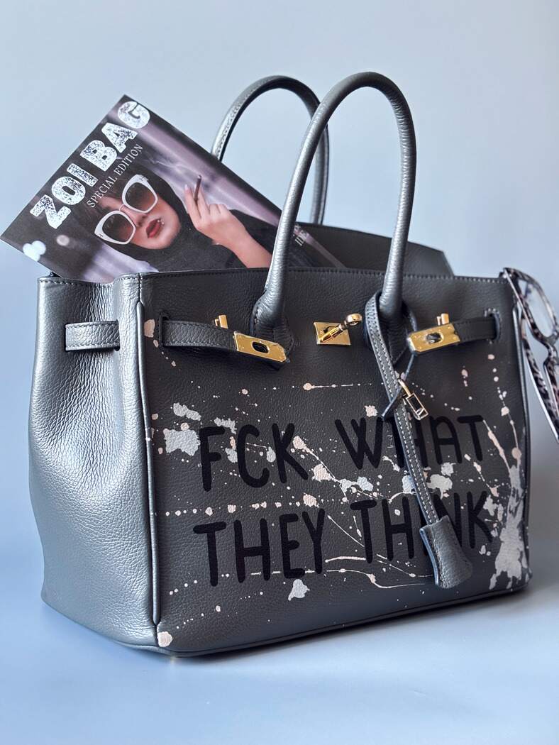 Designová luxusní šedá kožená kabelka Zoi Bag s ručně psaným nápisem a s cákanci barvou. Zapínání pomocí klíčku a zámku.