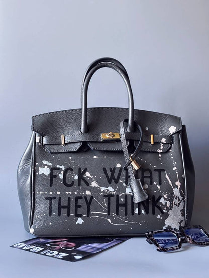 Designová luxusní šedá kožená kabelka Zoi Bag s ručně psaným nápisem a s cákanci barvou. Zapínání pomocí klíčku a zámku. Zapnutá.