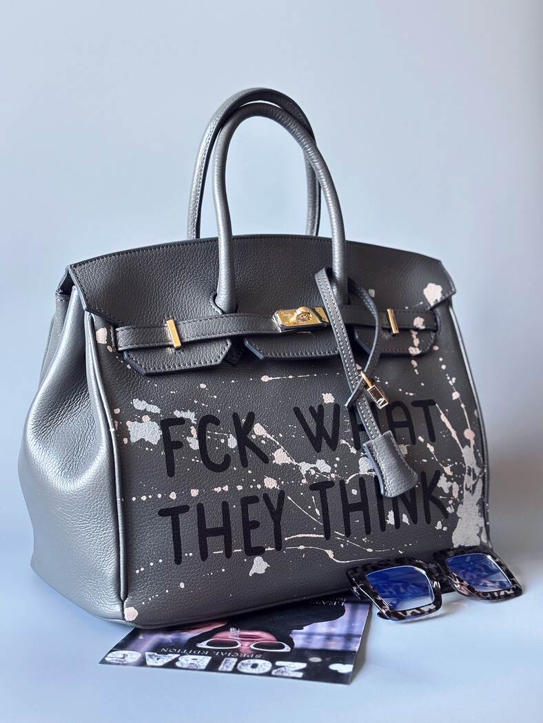 Designová luxusní šedá kožená kabelka Zoi Bag s ručně psaným nápisem a s cákanci barvou. Zapínání pomocí klíčku a zámku. Zapnnutá.