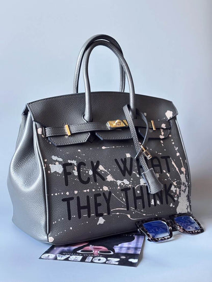 Designová luxusní šedá kožená kabelka Zoi Bag s ručně psaným nápisem a s cákanci barvou. Zapínání pomocí klíčku a zámku. Zapnnutá.