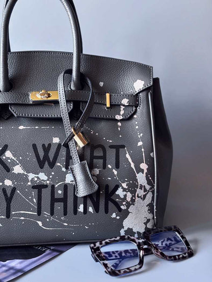 Designová luxusní šedá kožená kabelka Zoi Bag s ručně psaným nápisem a s cákanci barvou. Zapínání pomocí klíčku a zámku. Detail.