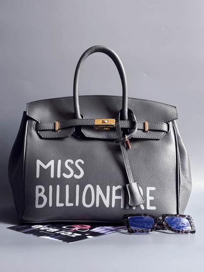 Šedá kožená kabelka Zoi Bag vyrobená z kvalitní italské kůže, s ručně psaným nápisem a se zámkem a klíčkem. Pro personalizaci na zakázku. Zapnutá.