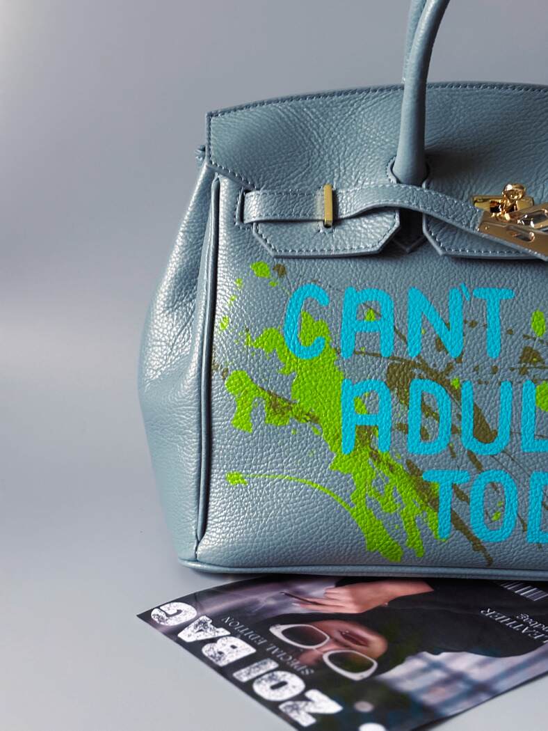 Šedá/modrá velká kožená kabelka Zoi Bag s ručně psaným nápisem "Can't adult today" a barevnými cákanci. Zlatý zámek s klíčkem.