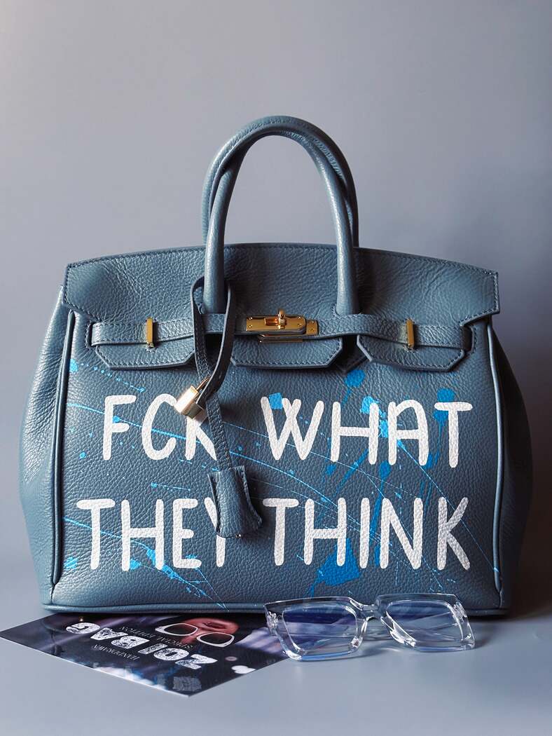 Velká kožená kabelka Zoi Bag v barevných tónech šedé a modré s ručně psaným bílým nápisem "FCK what they think" zapnutá