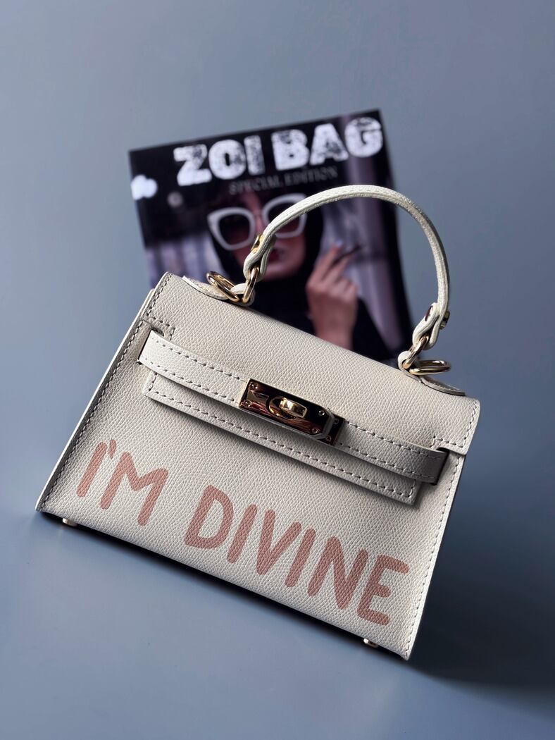 Designová luxusní světle béžová kabelka s ručně psaným nápisem, elegantním otočným zámkem a odnímatelným crossbody popruhem.