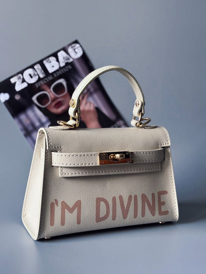Designová luxusní světle béžová kabelka s ručně psaným nápisem, elegantním otočným zámkem a odnímatelným crossbody popruhem.