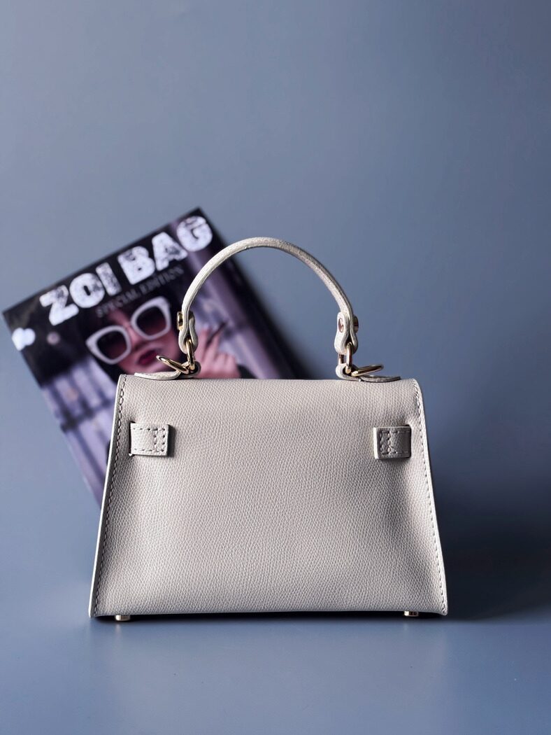 Designová luxusní světle béžová kabelka s ručně psaným nápisem, elegantním otočným zámkem a odnímatelným crossbody popruhem. Zezadu.