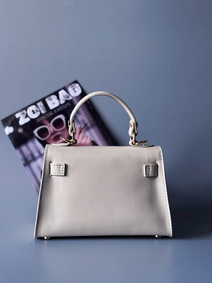 Designová luxusní světle béžová kabelka s ručně psaným nápisem, elegantním otočným zámkem a odnímatelným crossbody popruhem. Zezadu.