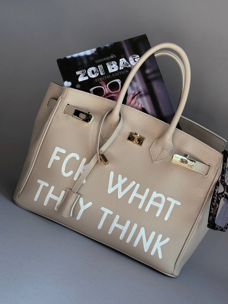 Světle béžová kožená shopper kabelka s ikonickým zapínáním na zámek a s originálním ručně malovaným nápisem.