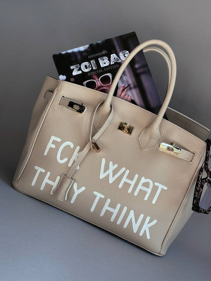 Světle béžová kožená shopper kabelka s ikonickým zapínáním na zámek a s originálním ručně malovaným nápisem.