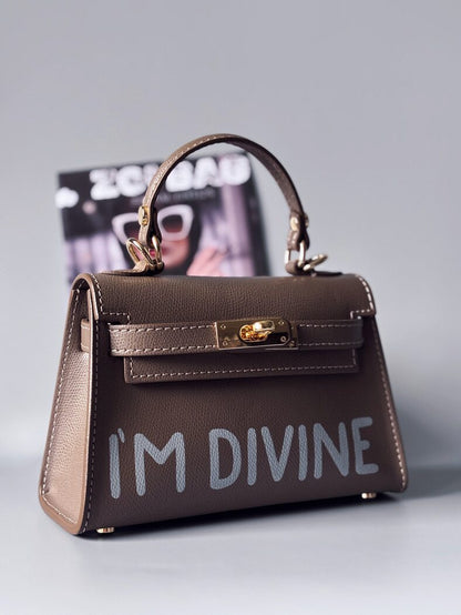 Designová luxusní tmavě béžová kabelka s ručně psaným nápisem, elegantním otočným zámkem a odnímatelným crossbody popruhem.