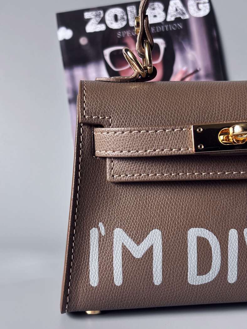 Designová luxusní tmavě béžová kabelka s ručně psaným nápisem, elegantním otočným zámkem a odnímatelným crossbody popruhem. Detail nápisu