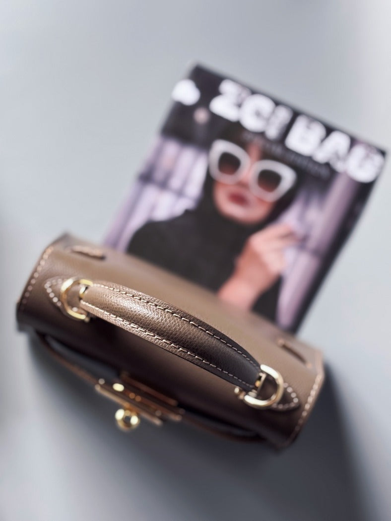 Designová luxusní tmavě béžová kabelka s ručně psaným nápisem, elegantním otočným zámkem a odnímatelným crossbody popruhem.