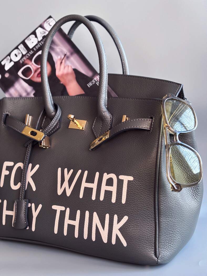 Designová luxusní kožená šedá kabelka Zoi Bag s ručně psaným nápisem. Ikonické zapínání na zámek s klíčkem.