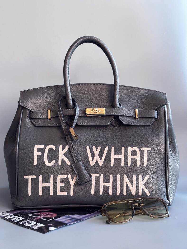 Designová luxusní kožená šedá kabelka Zoi Bag s ručně psaným nápisem. Ikonické zapínání na zámek s klíčkem. Zapnutá.
