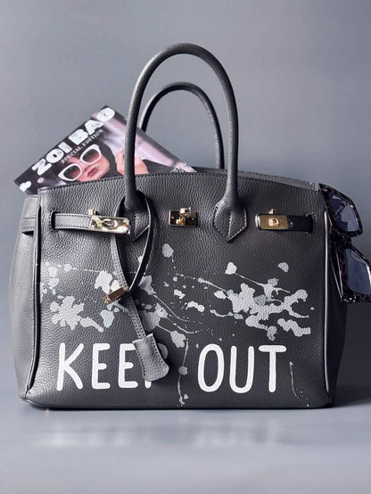 Luxusní designová kožená kabelka Zoi Bag s ručně psaným nápisem "Keep Out" a cákanci barvou. Zapínání pomocí zámku s klíčkem.
