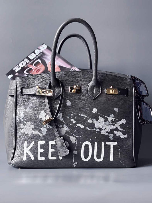 Luxusní designová kožená kabelka Zoi Bag s ručně psaným nápisem "Keep Out" a cákanci barvou. Zapínání pomocí zámku s klíčkem.