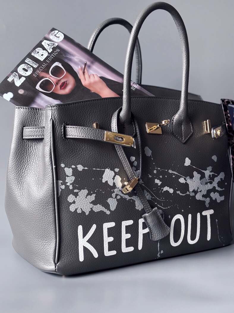 Luxusní designová kožená kabelka Zoi Bag s ručně psaným nápisem "Keep Out" a cákanci barvou. Zapínání pomocí zámku s klíčkem.