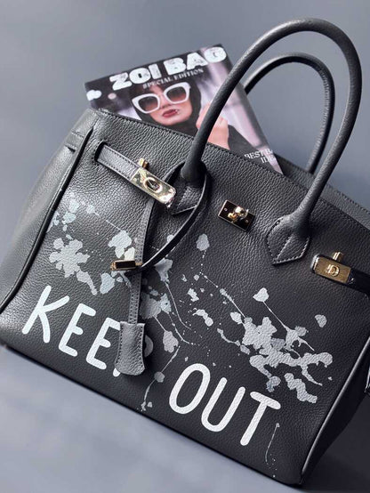 Luxusní designová kožená kabelka Zoi Bag s ručně psaným nápisem "Keep Out" a cákanci barvou. Zapínání pomocí zámku s klíčkem.