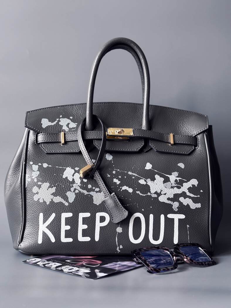 Luxusní designová kožená kabelka Zoi Bag s ručně psaným nápisem "Keep Out" a cákanci barvou. Zapínání pomocí zámku s klíčkem.