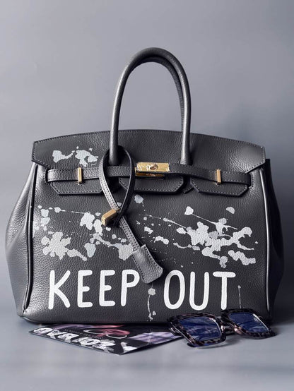 Luxusní designová kožená kabelka Zoi Bag s ručně psaným nápisem "Keep Out" a cákanci barvou. Zapínání pomocí zámku s klíčkem.