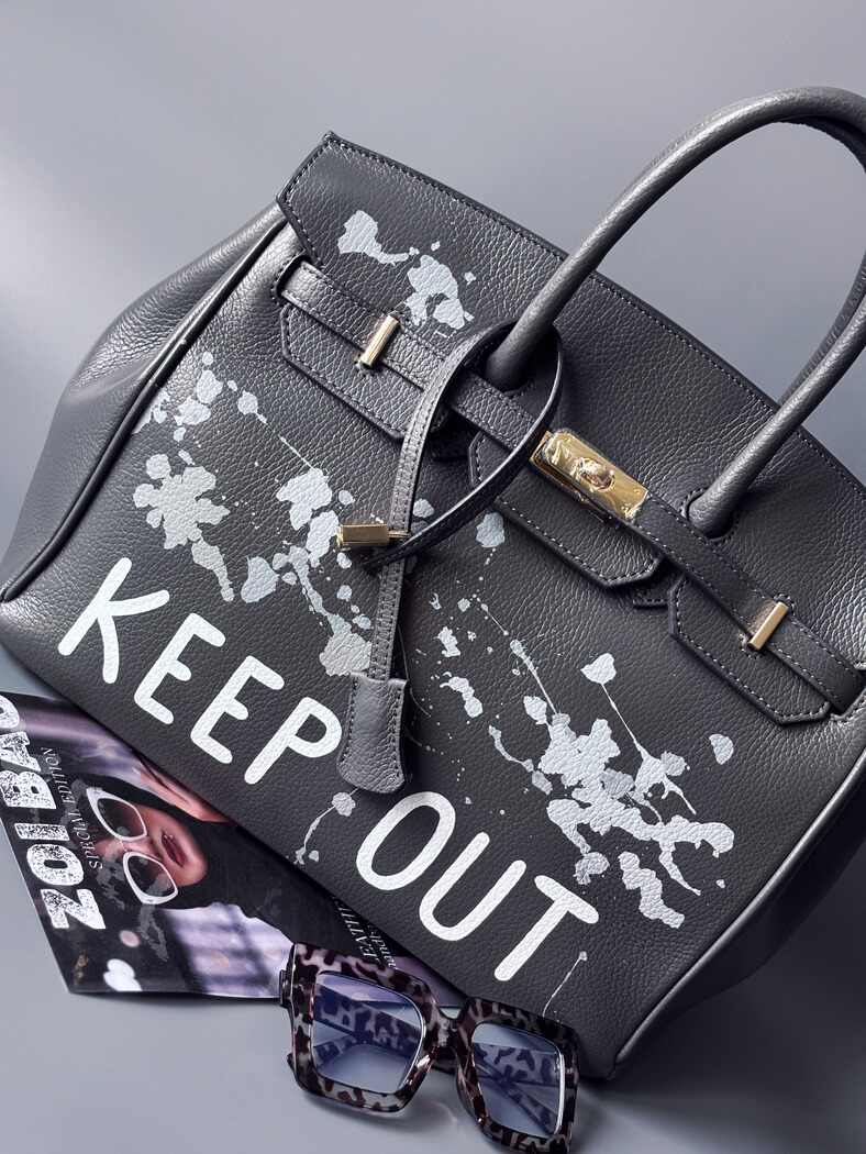 Luxusní designová kožená kabelka Zoi Bag s ručně psaným nápisem "Keep Out" a cákanci barvou. Zapínání pomocí zámku s klíčkem.