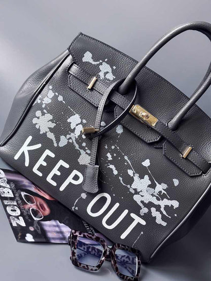 Luxusní designová kožená kabelka Zoi Bag s ručně psaným nápisem "Keep Out" a cákanci barvou. Zapínání pomocí zámku s klíčkem.