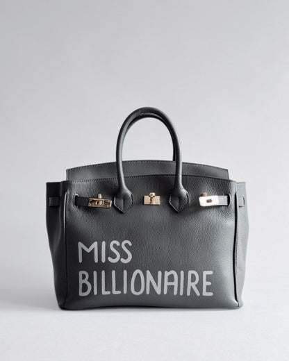 Šedá kabelka Moi z pravé italské kůže od značky Zoibag s ruční malbou “Miss Billionaire”, pohled zepředu.
