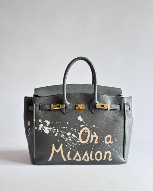 Šedá kabelka Nel s unikátní ruční malbou “On a Mission” od značky Zoibag z italské kůže, pohled zepředu.